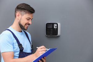 Male Technician With Clipboard Near Installed Alarm System Indoors